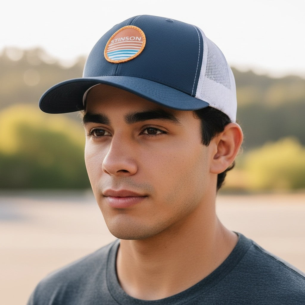 Lowkey Local navy and white trucker hat with a round Stinson sunset patch worn by a man outdoors.