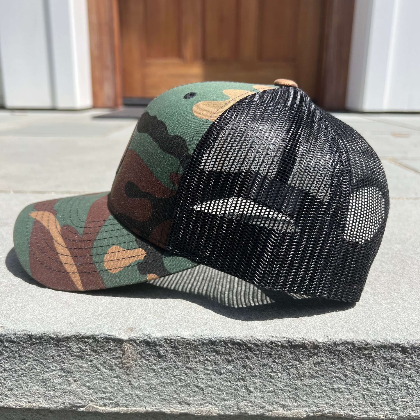 Lowkey Local camo trucker hat with black mesh back and structured 6-panel design on a stone surface