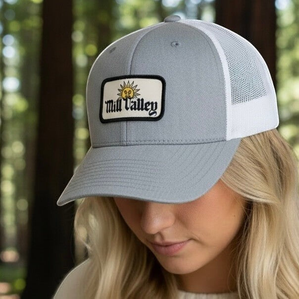 Lowkey Local Mill Valley trucker hat in heather gray with a white mesh back and sun patch detail worn by a woman.