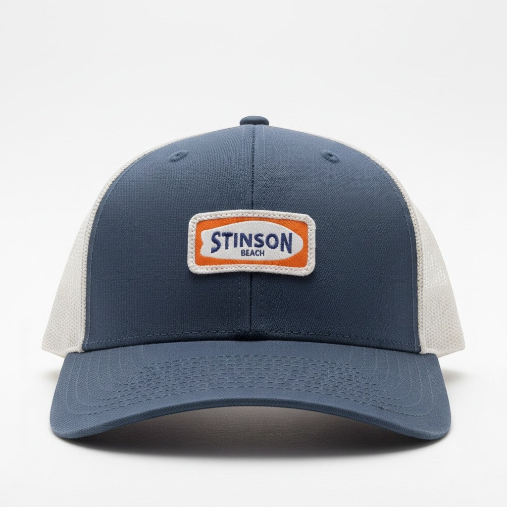 Lowkey Local navy blue trucker hat with a white mesh back and a rectangular Stinson Beach surf theme patch.