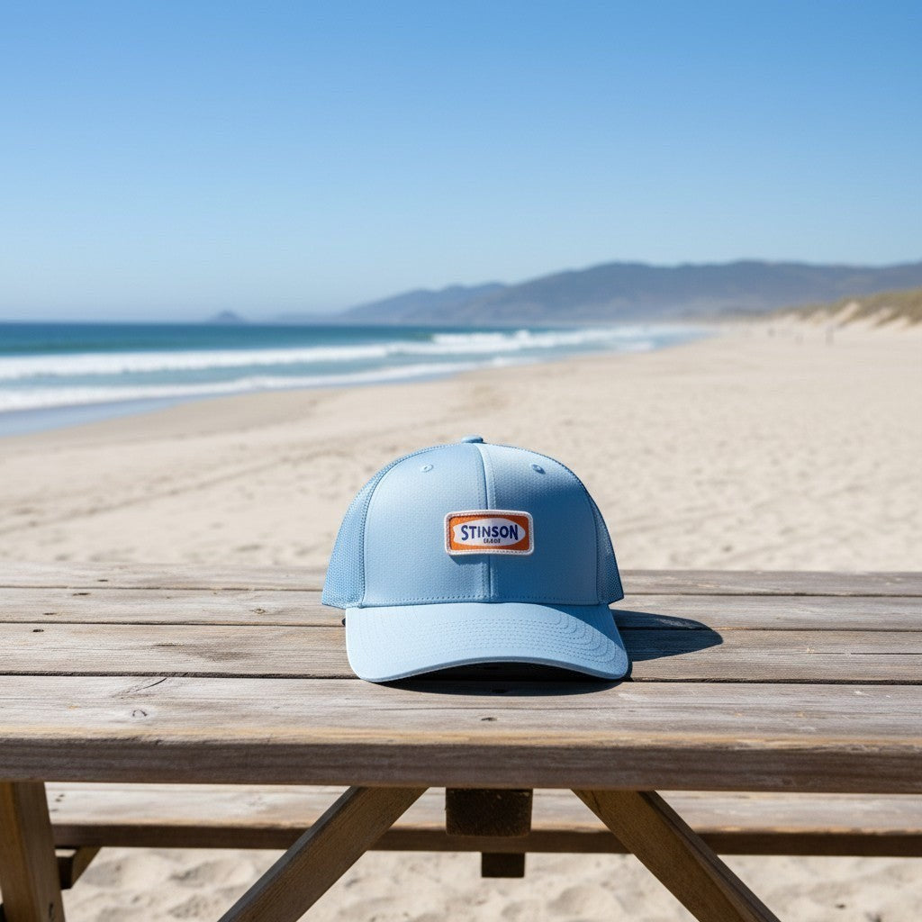 Lowkey Local Stinson Beach sky blue trucker hat on a wooden table at the beach
