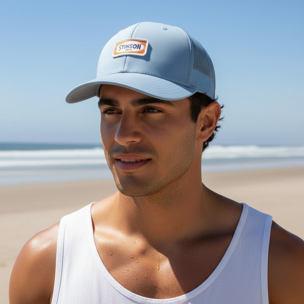 Lowkey Local Stinson Beach sky blue trucker hat with a rectangular patch worn by a man on a sunny beach