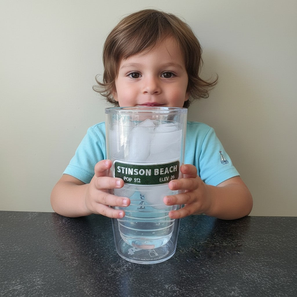 A child holding a clear Lowkey Local 16oz Tervis tumbler featuring a Stinson Beach graphic filled with ice water.