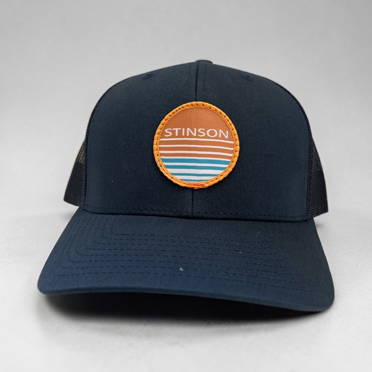 Lowkey Local Stinson Sunset navy trucker hat with a circular stitched patch featuring a sunset graphic