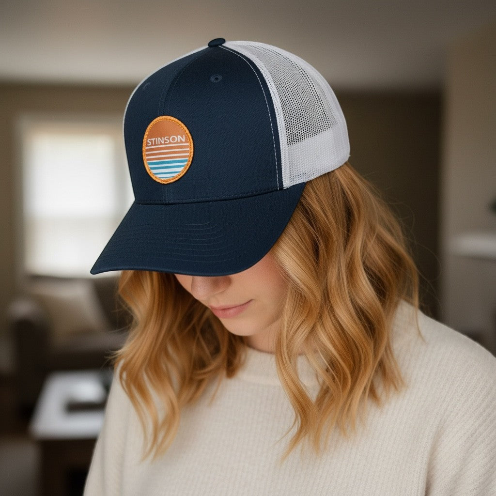Lowkey Local Stinson Sunset trucker hat in navy and white with a circular stitched patch, worn by a woman.